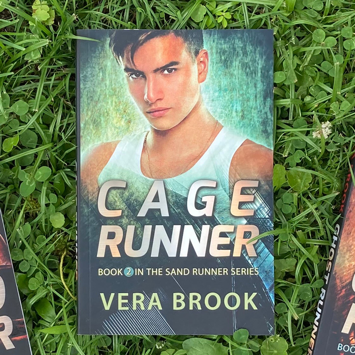 A paperback of Cage Runner, book in the Sand Runner Series by Vera Brook, on a very green grass.